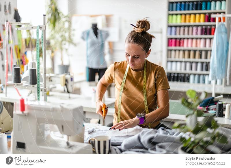 Junge Modedesignerin bei der Arbeit an ihrem Arbeitsplatz Handwerk Schneidern Herstellung handgefertigt Näherin Kleinunternehmen Nähmaschine Werkstatt Gewebe