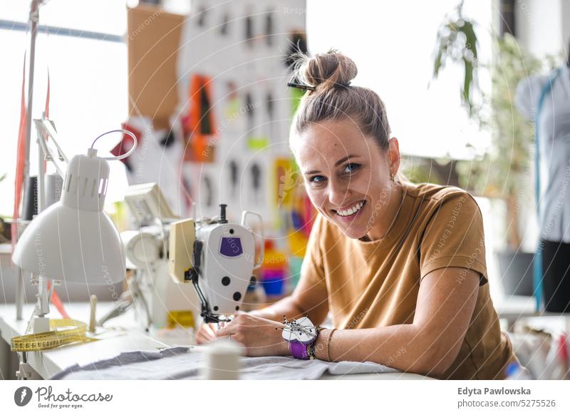 Modedesignerin an einer Nähmaschine an ihrem Arbeitsplatz Handwerk Schneidern Herstellung handgefertigt Näherin Kleinunternehmen Werkstatt Gewebe Hobby Nähen