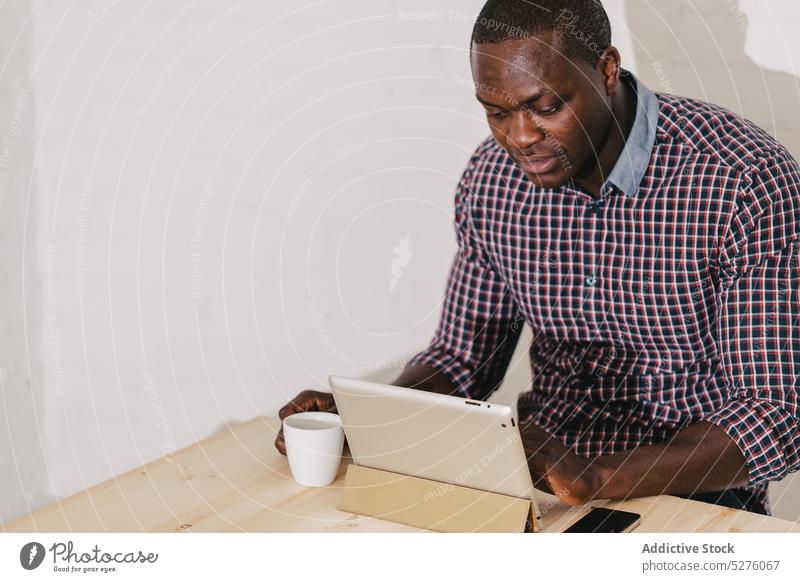 Konzentrierter schwarzer Mann bei der Arbeit mit einem digitalen Tablet auf einem Holztisch Erwachsener Afrikanisch Business Geschäftsmann selbstbewusst