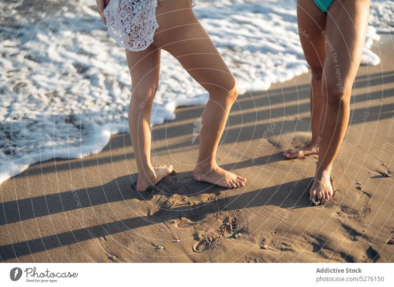 Crop Frauen stehen am Meer Freundin Strand MEER winken Sand Sommer Urlaub Wasser Wochenende Paar Zusammensein Küste Barfuß Freundschaft Feiertag schäumen