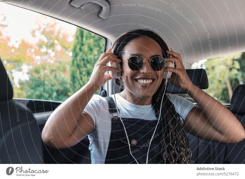 Lächelnde schwarze Frau mit Kopfhörern heiter PKW zuhören Musik benutzend Passagier Sonnenbrille Glück ethnisch Afroamerikaner jung Rücksitz Gerät Automobil