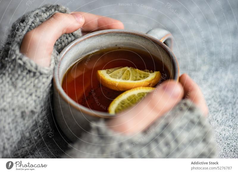Kinderhände halten eine Tasse Tee Hintergrund Getränk schwarz Zitrusfrüchte Nelken kalte Jahreszeit Beton lecker trinken grau Hand Gesundheit Halt heiß stricken