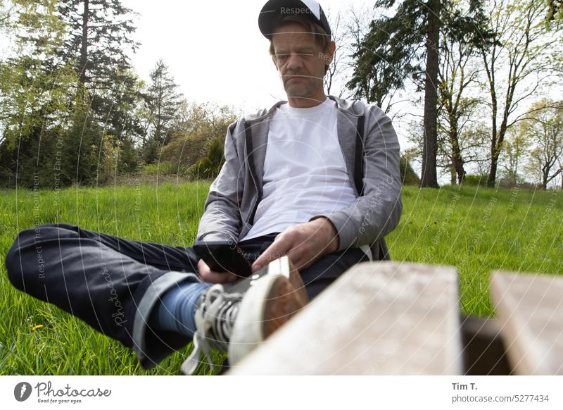 Sitzender Mann mit Telefon im Grünen Handy Natur sitzen Lifestyle Technik & Technologie Smartphone Mobile Mitteilung Mensch benutzend Funktelefon Gerät