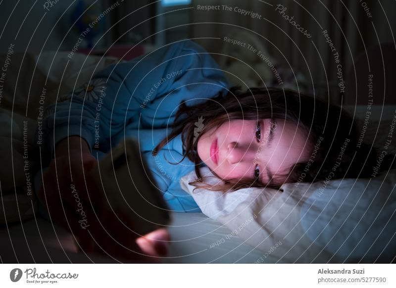 Ein Kind, das spät nachts im Bett liegt und sein Smartphone benutzt, Spiele spielt, Videos online anschaut und auf dem Bildschirm scrollt. Die Bildschirmsucht von Kindern. Das Kinderzimmer bei Nacht.