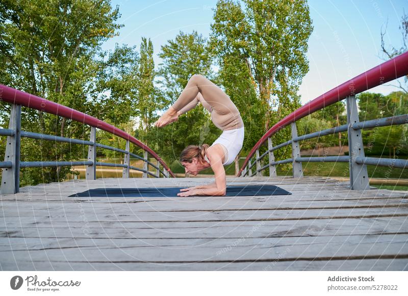 Sportliche Frau macht Yoga in Skorpionhaltung auf einer Brücke Asana Skorpion-Pose vrischikasana a Übung Gleichgewicht Athlet Motivation Park Sonnenlicht