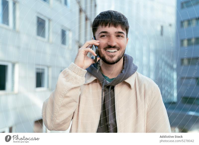 Lächelnder Mann, der in der Stadt mit seinem Smartphone spricht benutzend reden Telefonanruf Gespräch sprechen Straße urban diskutieren positiv männlich Typ