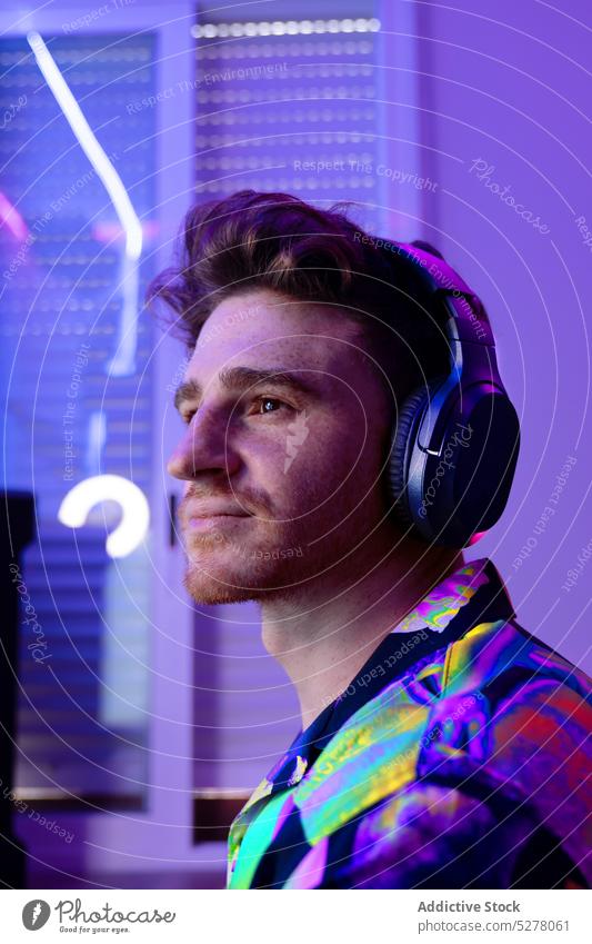 Nachdenklicher Mann mit Kopfhörern schaut weg verträumt nachdenklich Porträt neonfarbig Musik Drahtlos Stil farbenfroh Licht männlich jung zuhören Gerät