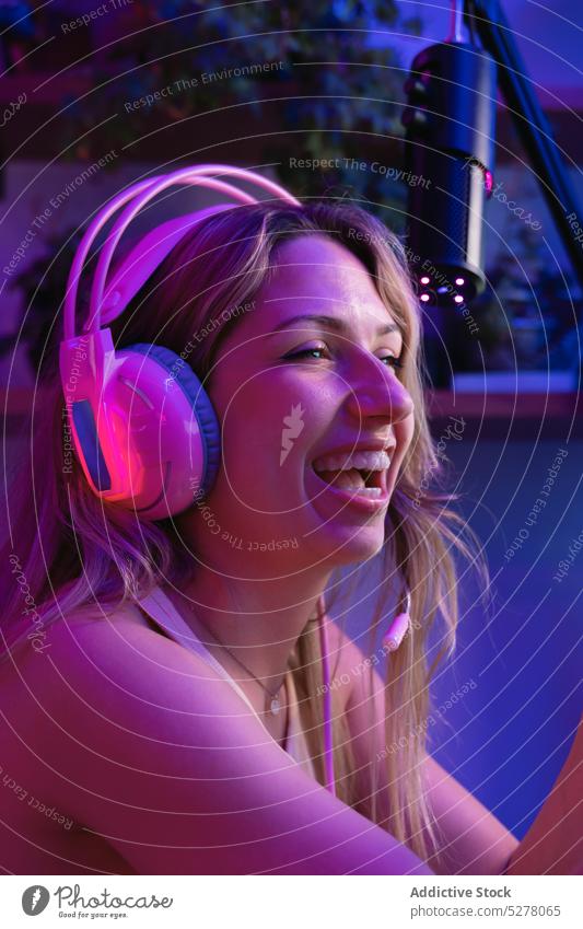 Fröhliche junge Frau mit Kopfhörern Lachen heiter Porträt Headset Gerät neonfarbig Apparatur rosa Licht dunkel Lächeln leuchten blond tausendjährig Glück