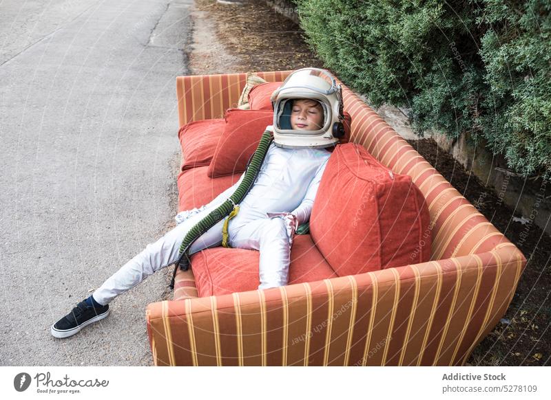 Kind im Raumanzug entspannt auf Sofa auf der Straße Junge Raumfahrer Kosmonaut Astronaut schlafen Liege Kälte ruhen Entdecker Schutzhelm Tracht Park Lügen