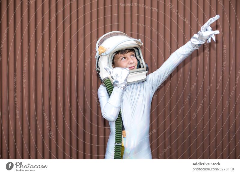 Junge im Raumanzug vor brauner Wand Kind Kosmonaut Astronaut Aufmerksamkeit erkunden neugierig zeigen Überraschung stehen Interesse Schutzhelm Zeigefinger