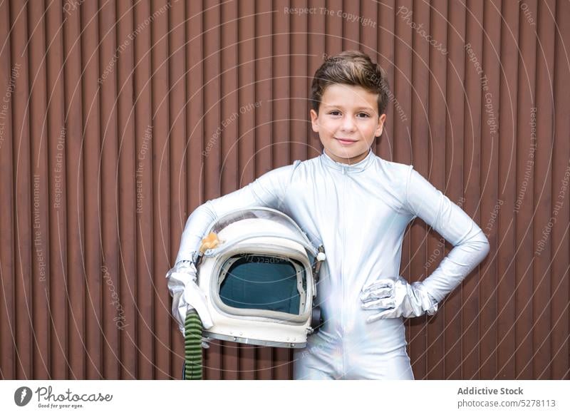 Kind im Raumanzug an brauner Wand stehend Junge Kosmonaut Astronaut Raumfahrer Entdecker Schutzhelm Gras verdorren futuristisch Tracht Zukunft altmodisch