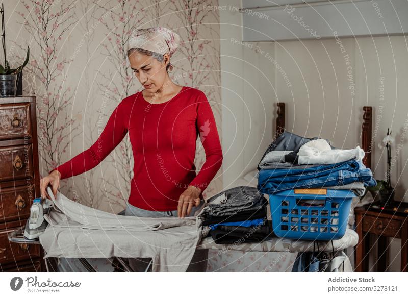 Ältere Frau faltet Kleidung im Zimmer bügeln Haushalt Stoff heimwärts Hausarbeit heimisch Routine Falten Arbeit ethnisch Hausfrau gealtert vorbereiten