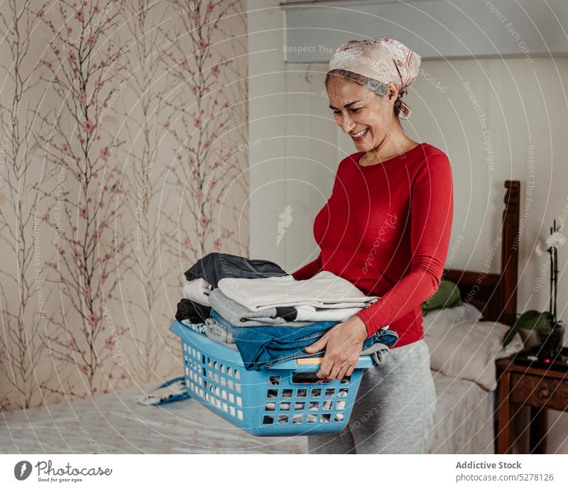 Fröhliche Frau trägt Korb mit Kleidung Hausfrau Wäscherei Lächeln führen Arbeit Stoff Routine Glück Hausarbeit positiv Haushalt heimwärts heiter Hygiene