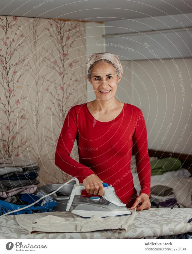 Lächelnde ältere Frau beim Bügeln von Hosen bügeln Haushalt Hausfrau Arbeit heimisch heimwärts Hausarbeit Routine Stoff reif lässig heiter Glück Haushälterin