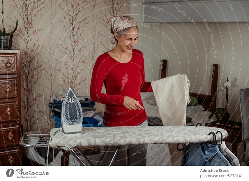 Lächelnde ältere Frau beim Bügeln von Hosen bügeln Haushalt Hausfrau Arbeit heimisch heimwärts Hausarbeit Routine Stoff reif lässig heiter Glück Haushälterin