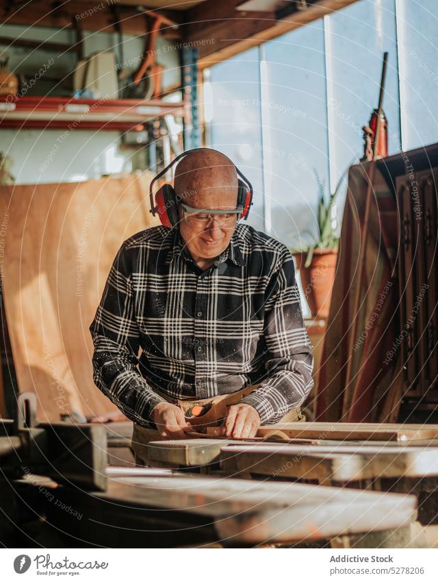 Zimmermann schneidet Holz in der Werkstatt Mann Zimmerer Holzarbeiten hölzern geschnitten Schreinerei Tischlerarbeit Schiffsplanken professionell Kopfhörer