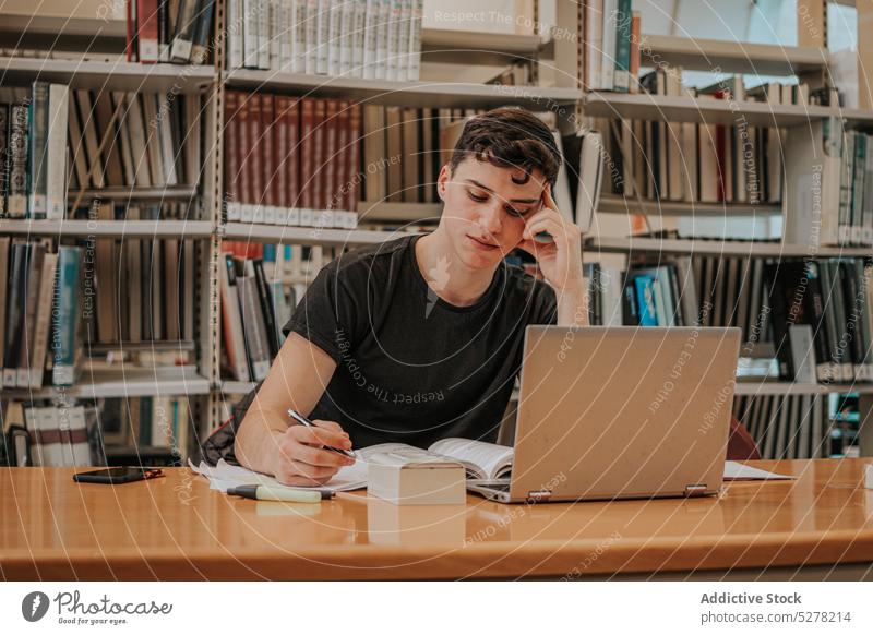 Konzentrierter männlicher Student, der sich in der Bibliothek auf eine Prüfung vorbereitet Mann Hausaufgabe Laptop Schüler schreiben zur Kenntnis nehmen Wissen