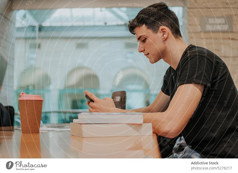 Konzentrierter Teenager beim Surfen auf dem Smartphone im Café Mann Buch Schüler Textnachricht Kaffee Browsen lernen Konzentration männlich Tisch Imbissbude