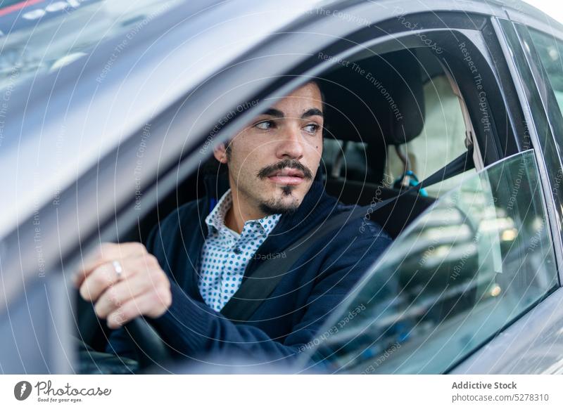 Junger hispanischer männlicher Fahrer in einem modernen Auto sitzend Mann Laufwerk PKW Konzentration Fahrzeug Lenkrad selbstbewusst Großstadt Fenster ernst jung