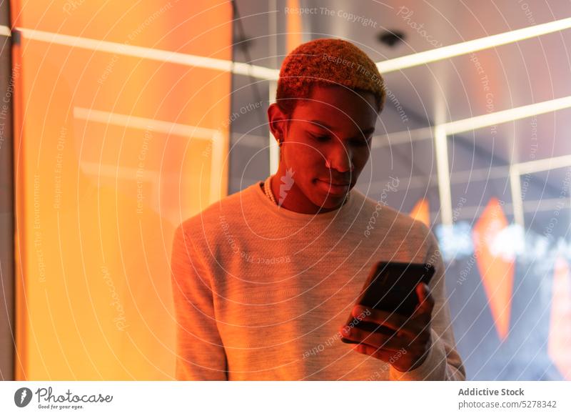 Seriöser schwarzer Mann mit Smartphone Browsen benutzend Nachricht neonfarbig Konzentration Fokus ernst Gerät männlich jung ethnisch Apparatur lässig Mobile