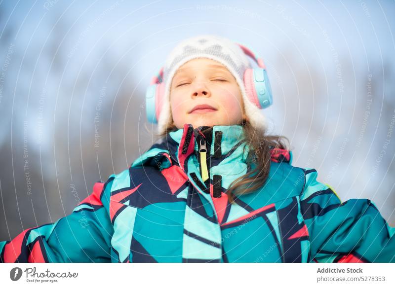 Ruhiges Mädchen, das mit Kopfhörern Musik hört zuhören Winter Inhalt Augen geschlossen warme Kleidung kalt Lächeln Hut Melodie Oberbekleidung Kind Audio Gesang