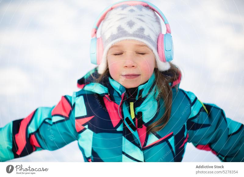 Ruhiges Mädchen, das mit Kopfhörern Musik hört zuhören Winter Inhalt Augen geschlossen warme Kleidung kalt Lächeln Hut Melodie Oberbekleidung Kind Audio Gesang