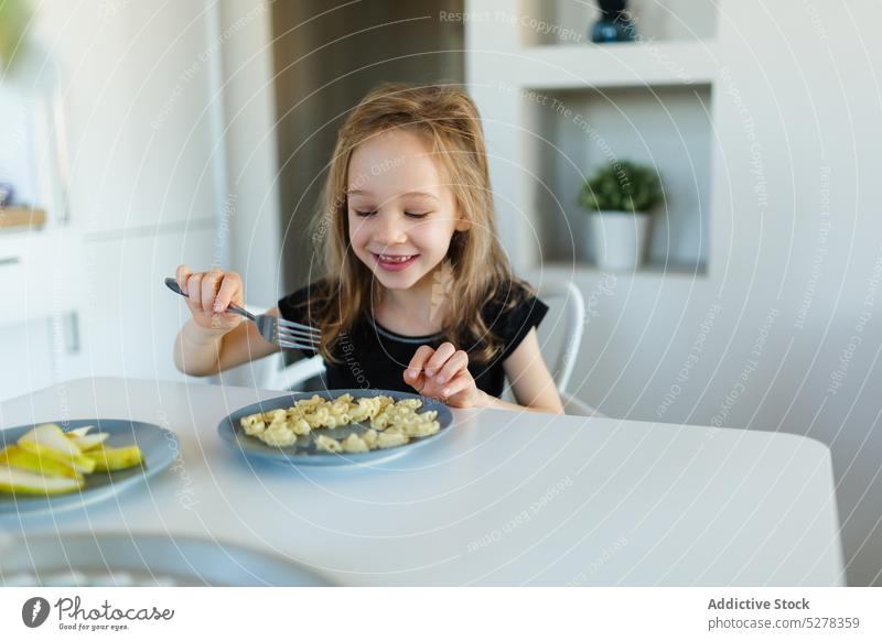 Glückliches Vorschulmädchen isst Nudeln am Tisch Mädchen Kind Ernährung nähren essen Lächeln Lebensmittel Spätzle Nährstoff Kindheit Teller Inhalt niedlich