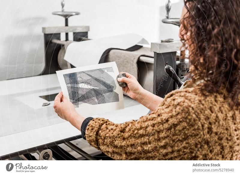 Anonyme Kunsthandwerkerin bei der Prüfung gravierter Fotos Handwerkerin untersuchen Fotogravur Papier handgefertigt Tisch Atelier Frau reif Werkstatt Hobby
