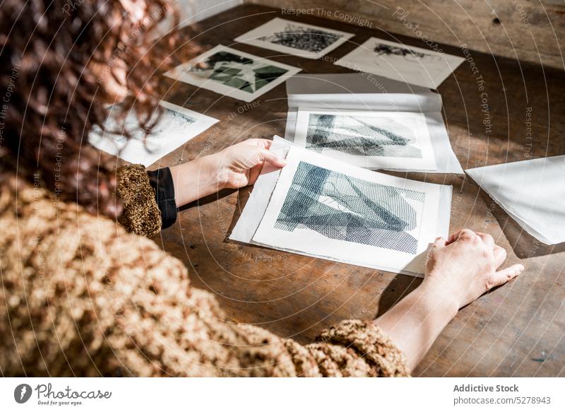 Anonyme Kunsthandwerkerin bei der Prüfung gravierter Fotos Handwerkerin untersuchen Fotogravur Papier handgefertigt Tisch Atelier Frau reif Werkstatt Hobby