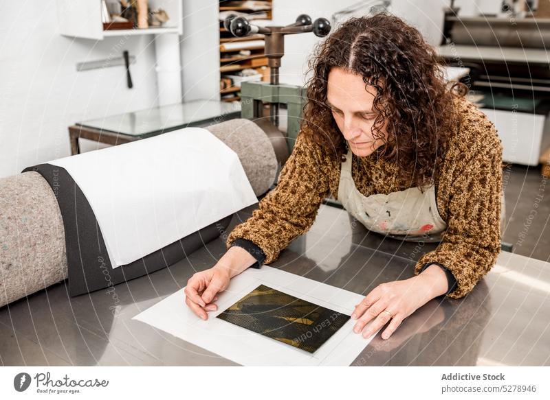 Handwerkerin mittleren Alters, die eine Fotogravurplatte auf Papier anordnet Teller Tisch ausrichten Schot Ornament abstrakt Werkstatt Frau Lebensmitte reif