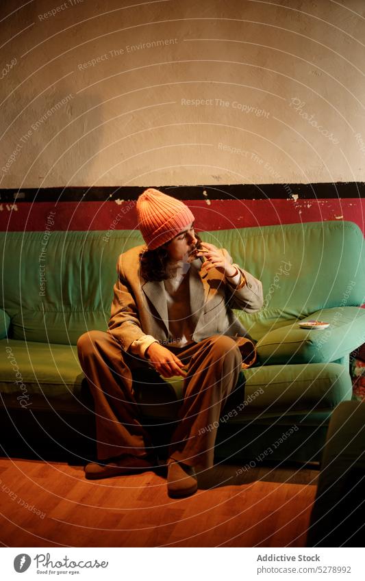 Stilvoller ethnischer Mann raucht Zigarette auf Couch Rauch Sofa Tabak Kälte Süchtige inhalieren ausatmen Habitus männlich hispanisch jung ruhen selbstbewusst