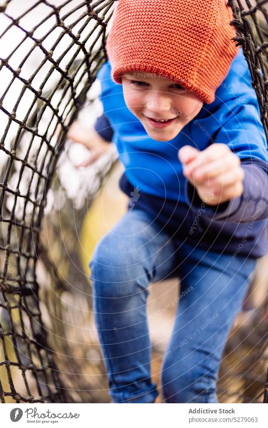 Glücklicher Junge, der auf dem Spielplatz im Netz läuft Kind Lächeln Wochenende positiv Freude Kindheit Spaß haben spielen Hut heiter Spaziergang bezaubernd