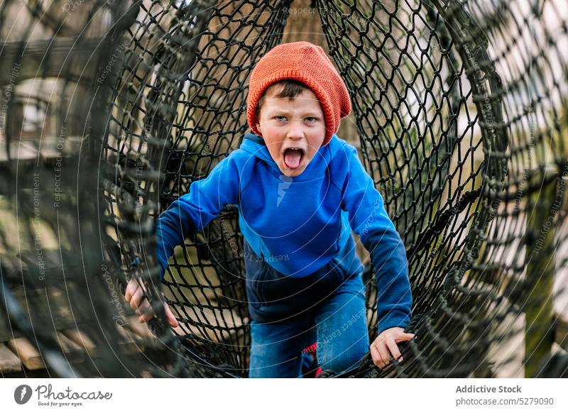 Lustiger Junge klettert auf Netz im Park Spielplatz spielen Aufstieg spielerisch Freude Spaß haben Vergnügen Wochenende Kind Kindheit Aktivität Glück