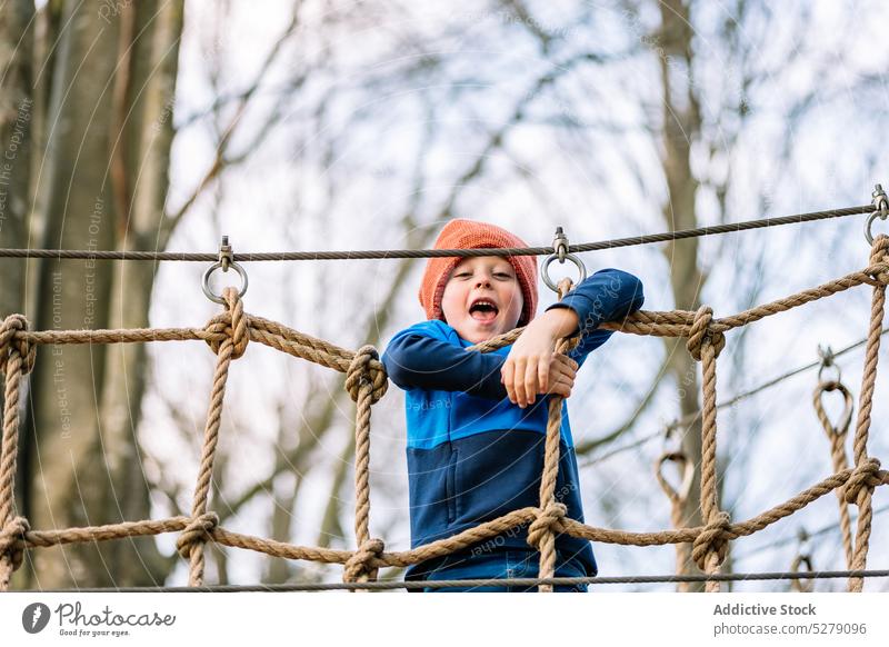 Lächelnder Junge klettert auf dem Spielplatz auf ein Netz Park Aufstieg Herbst Seil Zeitvertreib Wochenende spielen Vergnügen Kind Glück heiter Aktivität Freude