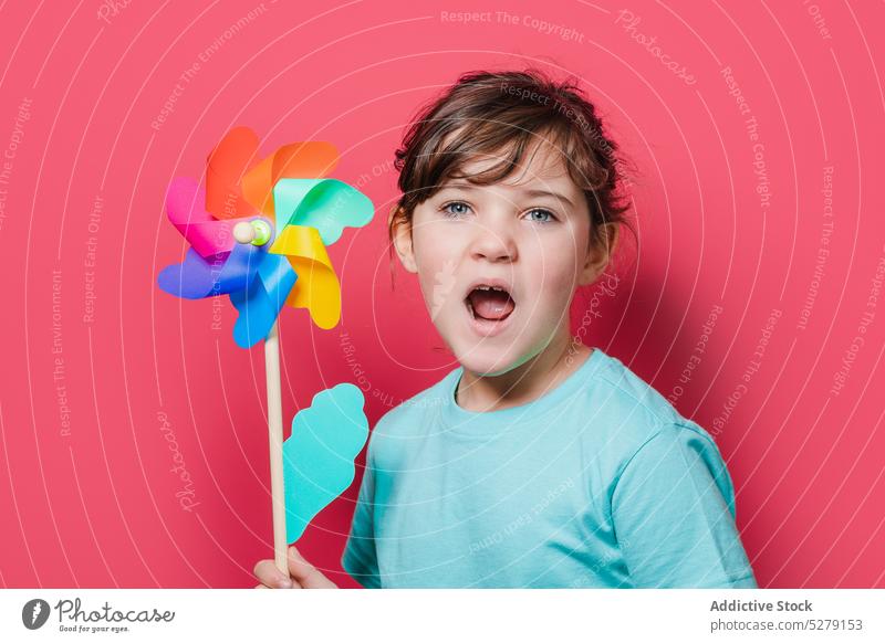 Nettes Mädchen hält Windrad und schaut in die Kamera Kind Regenbogen Blume Halt Blütenblatt spielen offener Mund Freizeit unterhalten lustig spielerisch