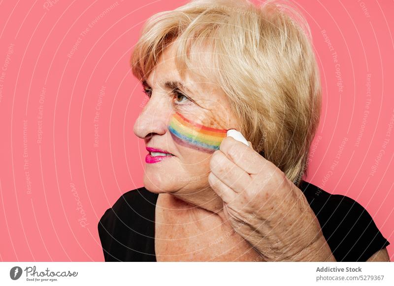 Ältere Frau malt Regenbogen auf Gesicht Porträt zeichnen farbenfroh positiv kreativ hell Lächeln Farbe Glück in den Ruhestand gehen Kunst heiter Rentnerin älter