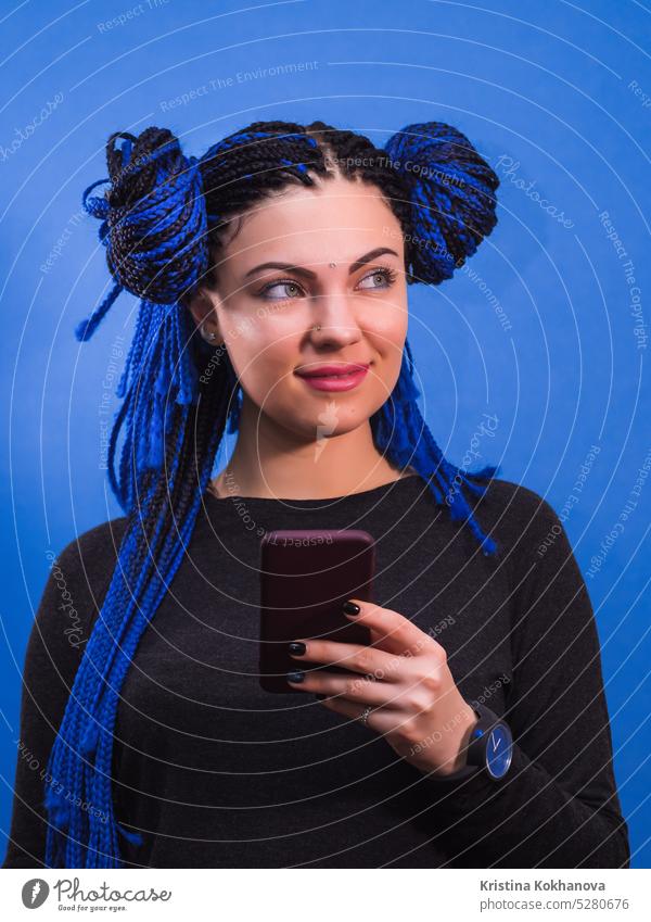 Adorable Hipster kaukasische Frau mit afrikanischen bunten Zöpfen Frisur stehend mit Handy, lächelnd, posiert auf blaue Wand schön Mädchen Mobile Porträt hübsch