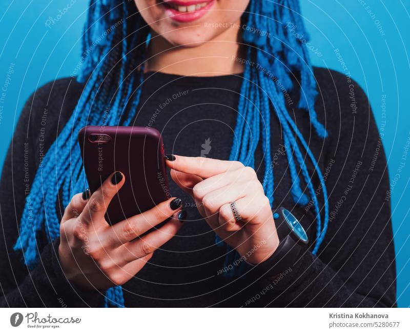 Adorable Hipster kaukasische Frau mit afrikanischen bunten Zöpfen Frisur Überprüfung News-Feed oder Messaging über soziale Netzwerke, mit kostenlosen Wi-Fi auf Handy, lächelnd, posiert auf blaue Wand