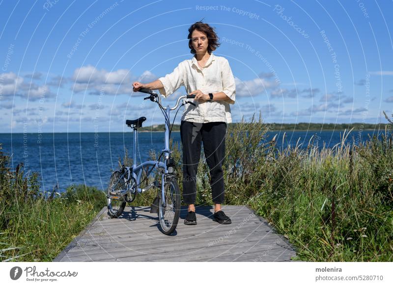 Junge Frau steht mit ihrem Fahrrad Fahrradfahren Radfahren Lifestyle Mitfahrgelegenheit Freizeit aktiv Aktivität Großstadt Park lockig Sommer im Freien