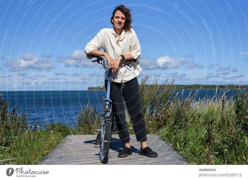 Junge Frau steht mit ihrem Fahrrad Fahrradfahren Radfahren Lifestyle Mitfahrgelegenheit Freizeit aktiv Aktivität Großstadt Park lockig Sommer im Freien