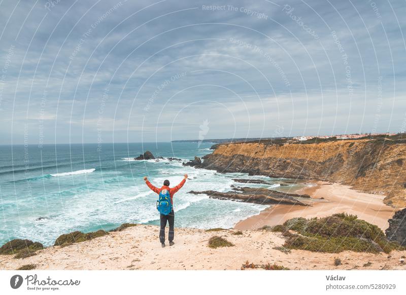 Rucksacktourist genießt seine Wanderung auf dem Fisherman Trail, Portugal. Blick auf den Strand Alteirinhos bei Zambujeira do Mar, Region Odemira. Atlantischer Ozean, felsige Klippen und Strand