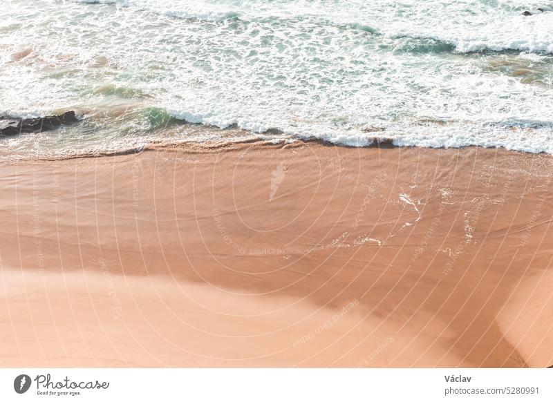 Sanft fließende, blaugrüne Wellen an einem gelben Sandstrand in der Region Odemira, Westportugal. Wanderung entlang des Fischerpfads, Rota Vicentina Portugal