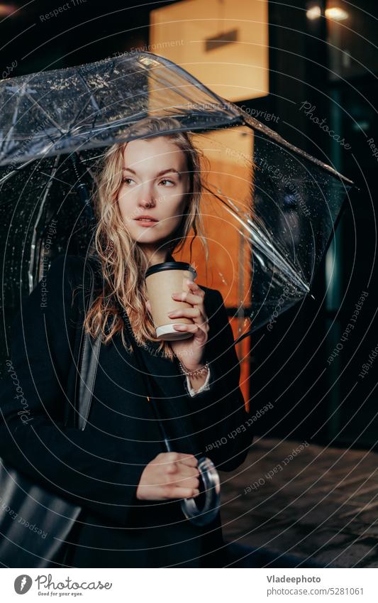 Blonde Frau im Mantel geht unter Regenschirm und hält Pappbecher in der Stadt Tasse Beteiligung Stehen Papier Wetter herbstlich Kaffee unten Erwachsener