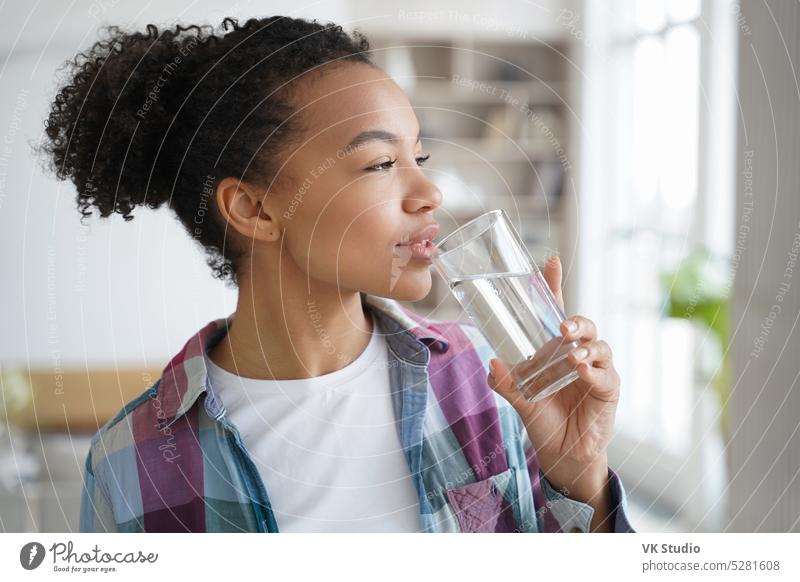 Gemischte Rasse junges Mädchen trinken reines Wasser aus Glas zu Hause. Gesunder Lebensstil, Morgenroutine biografisch Wellness Halt Afro-Look Diät abnehmen