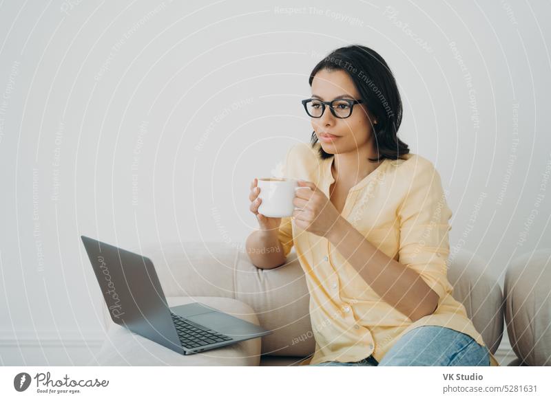 Nachdenkliche weibliche Geschäftsfrau arbeitet online an einem Laptop und hält eine Tasse Kaffee im Heimbüro. Fernarbeit Frau Geschäftsmann Arbeit e-Commerce