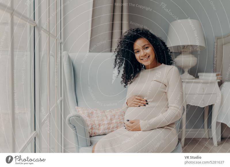 Positive schwangere Frau, die sanft ihren Bauch berührt und lächelt Afrikanisch gemischte Rasse jung Glück Baby Liebe Kind Unterleib Mutterschaft Mama Eltern