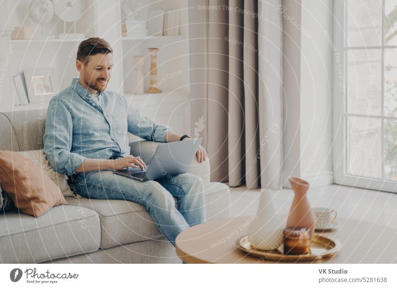 Junge attraktive lächelnde Freiberuflerin, die auf einem bequemen Sofa zu Hause arbeitet Mann aus der Ferne arbeiten online heimwärts Laptop Sitzen gemütlich