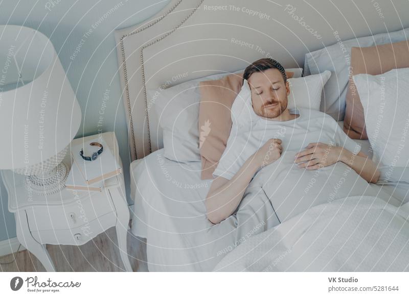 Hübscher junger bärtiger Mann schläft in einem geräumigen bequemen Bett schlafen Mittagsschlaf Morgen Schlafzimmer gemütlich Glück gutaussehend Streu