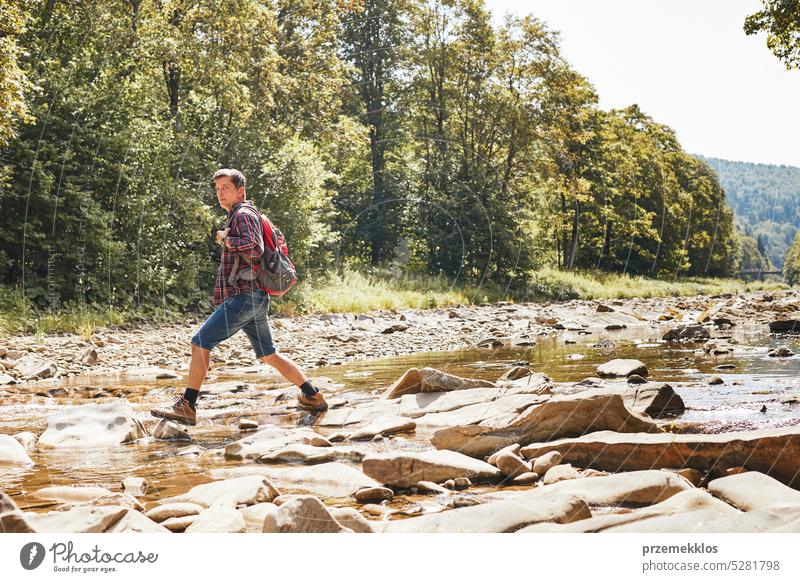 Trekking mit Rucksack Konzeptbild. Backpacker trägt Trekking-Stiefel überqueren Berg Fluss. Mann Wandern in den Bergen während der Sommerreise Abenteuer reisen