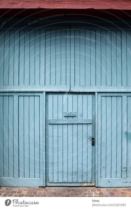 MainFux | Hintereingang Tür Tor blau Holz Eingang Straßenpflaster überdacht Hotel Herberge Tourismus Unterkunft Dachüberstand alt mächtig lädiert abgenutzt